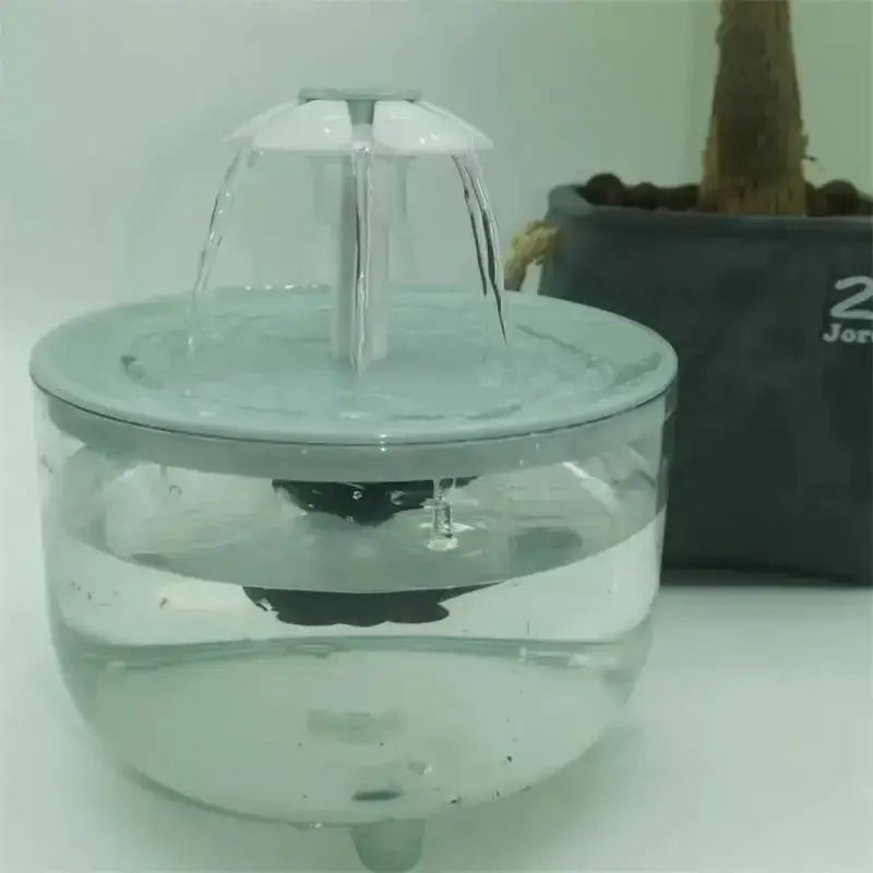 klarer Kunststoff-Automatik-Trinkwasserspender für Haustiere mit grauem Deckel, weißem Wasserauslauf und zentraler Pumpe, die eine sanfte Wasserfallwirkung erzeugt.