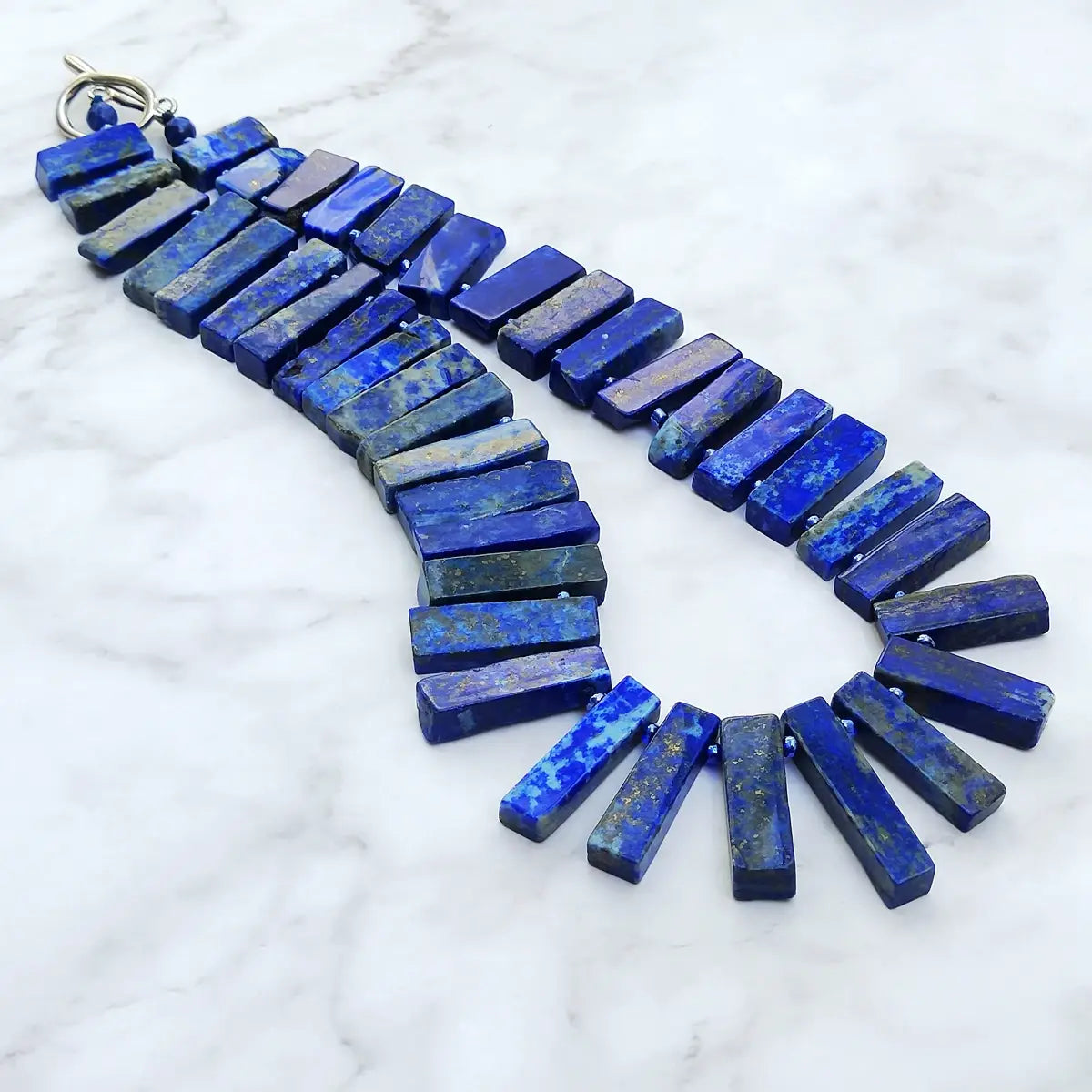 Un collier ras du cou audacieux en lapis-lazuli bleu royal, présentant des perles de pierres précieuses et une fermeture à bascule à tons argentés, pièce de bijouterie de déclaration.