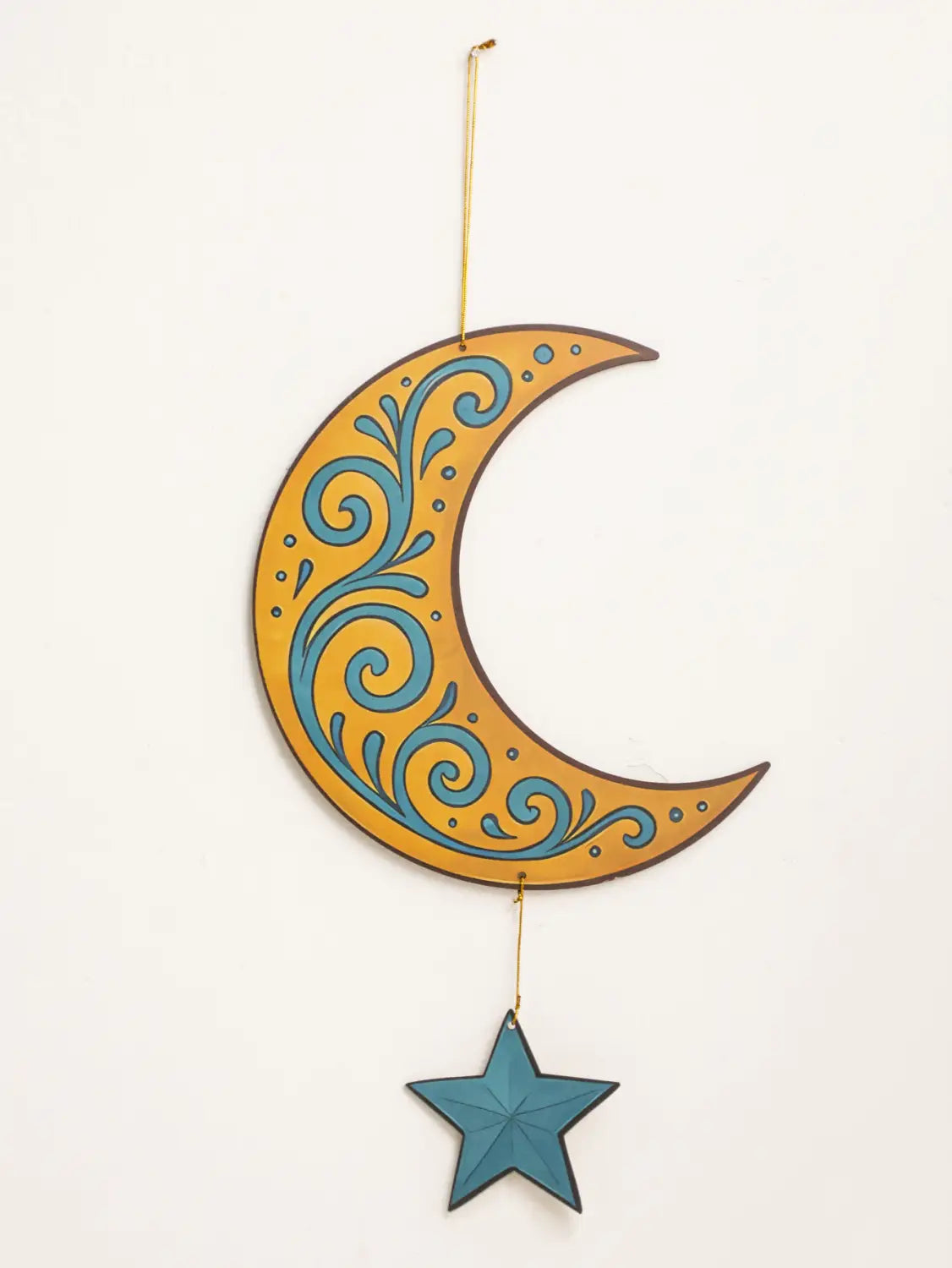 Un farol de luna y estrella para decoración de pared de Ramadán islámico en estilo moderno, con un adorno colgante de media luna decorada con remolinos teal sobre un fondo dorado, suspendido mediante una fina cuerda dorada, por encima de una estrella azul a juego.