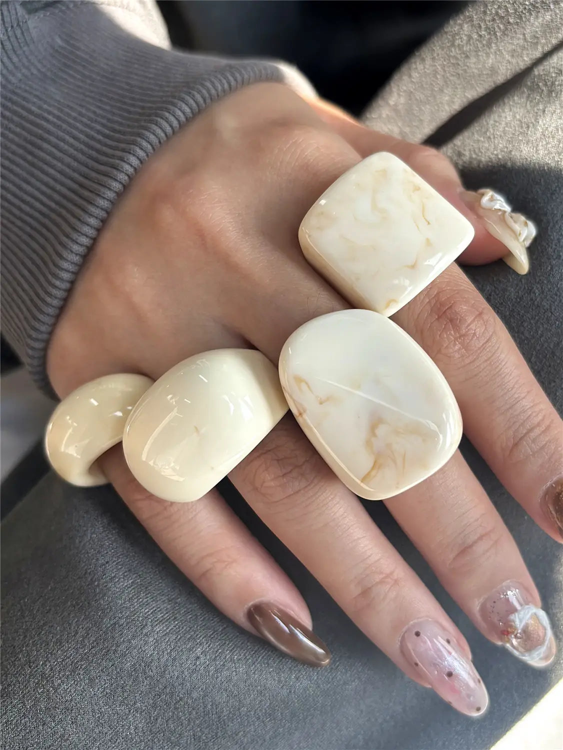 Cream-colored marbled resin chunky cocktail rings with smooth rounded edges worn on multiple fingers in a four-piece set.
