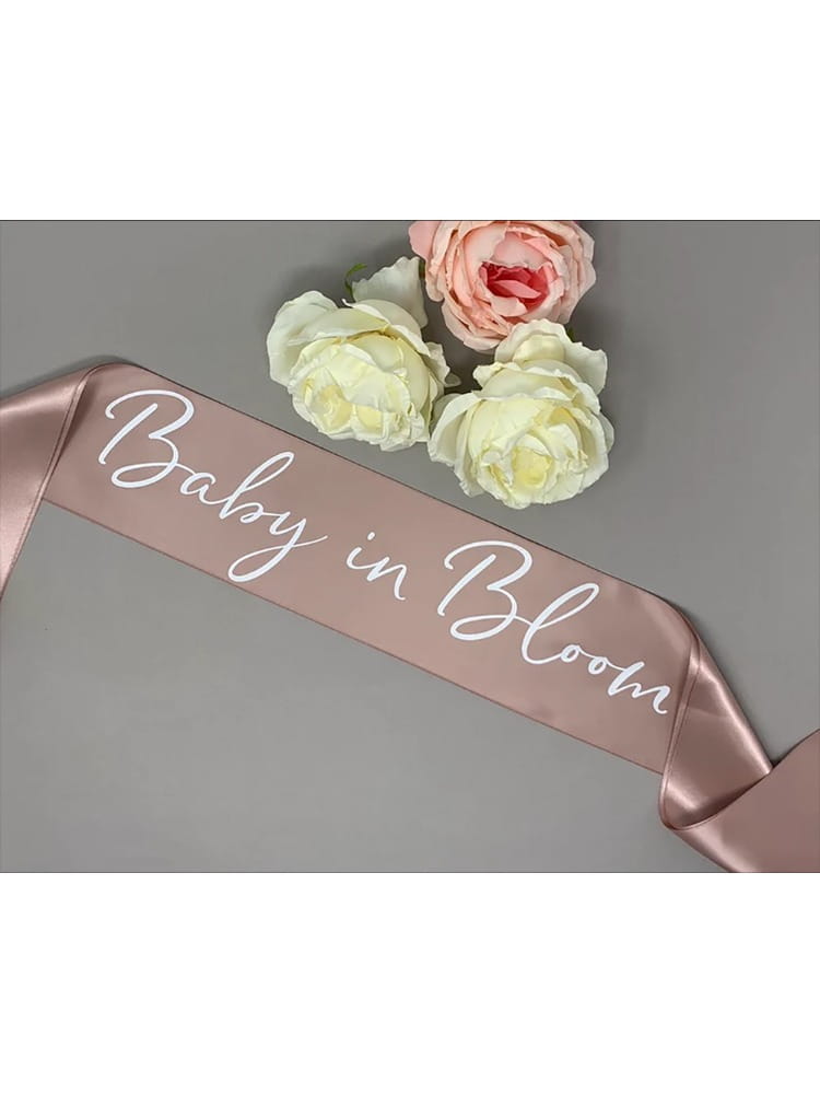 Une écharpe de baby shower en satin rose doré pâle avec « baby in bloom » écrit en script cursif blanc, pour la future maman, en satin blush rose pâle, à utiliser.