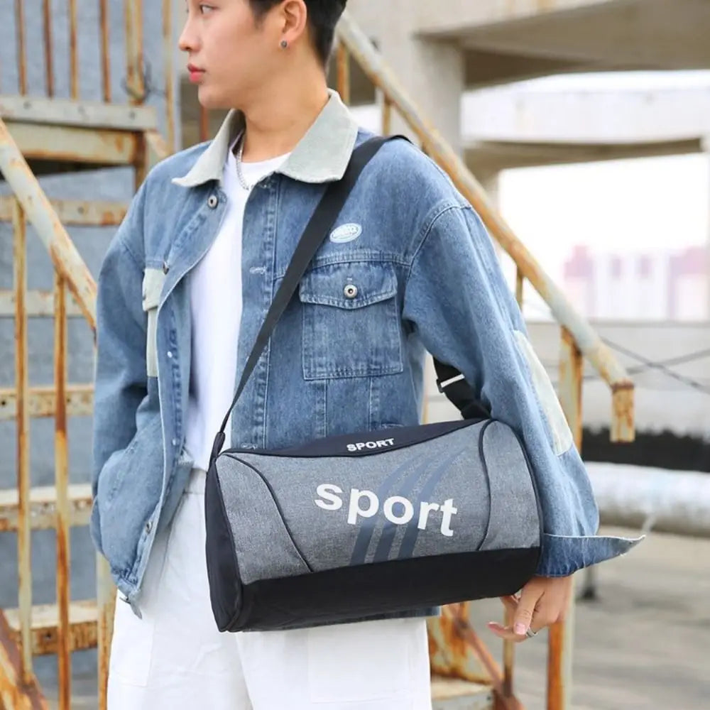 Bolsa deportiva tipo duffel pequeña gris y negra con letrero deportivo blanco, diseñada para entrenamientos de gimnasio y aptitud física y para uso de mano.