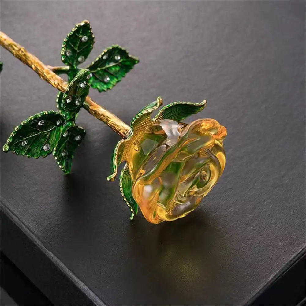A translucent amber crystal glass rose gift for Valentine’s Day with green enamel leaves, a gold-toned stem, and sparkling rhinestones.