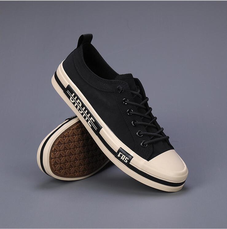 Baskets décontractées en toile pour hommes, chaussures d’été légères en noir, avec un design bas, une coque et une semelle en caoutchouc couleur crème, des lacets noirs et une inscription blanche sur le côté.