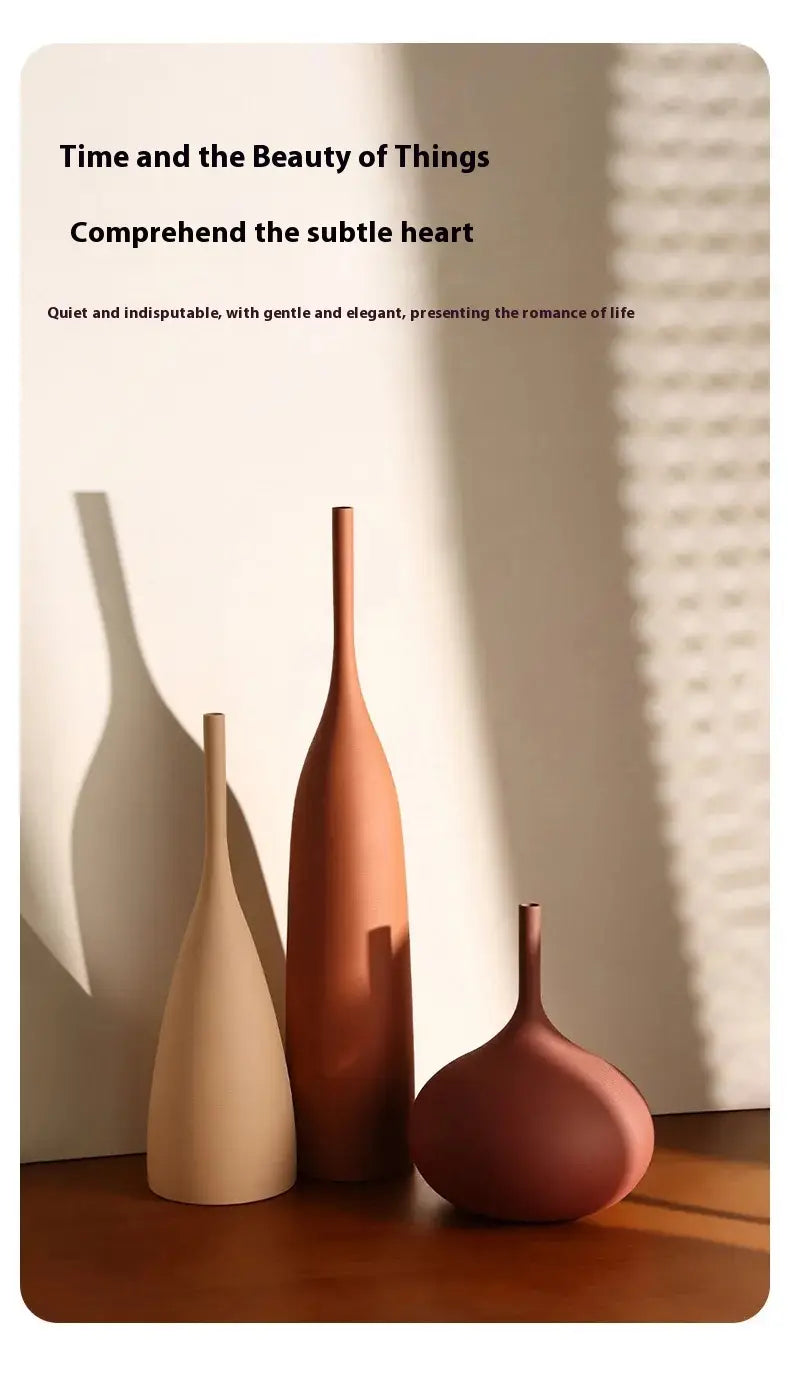 Tres jarrones de cerámica minimalistas en tonos tierra beige terracota y rojo apagado se encuentran con elegancia sobre una superficie de madera, como parte de un conjunto de jarrones de cerámica minimalista para una decoración wabi sabi.