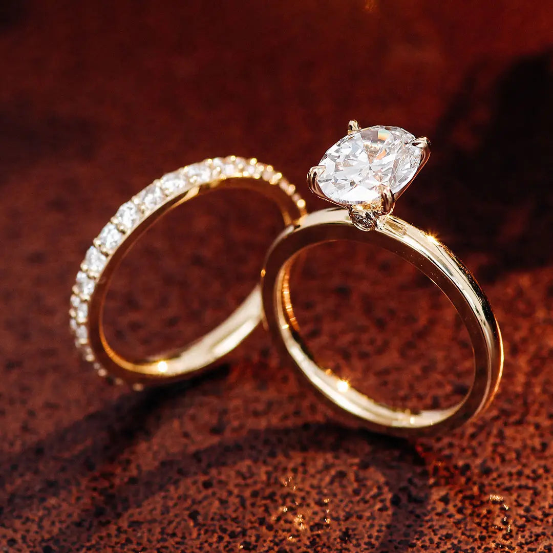Ensemble de bague de fiançailles en diamant de laboratoire ovale, ton or, comprenant une bague de fiançailles avec un diamant ovale proéminent maintenu par quatre griffes et une alliance assortie ornée de diamants plus petits.