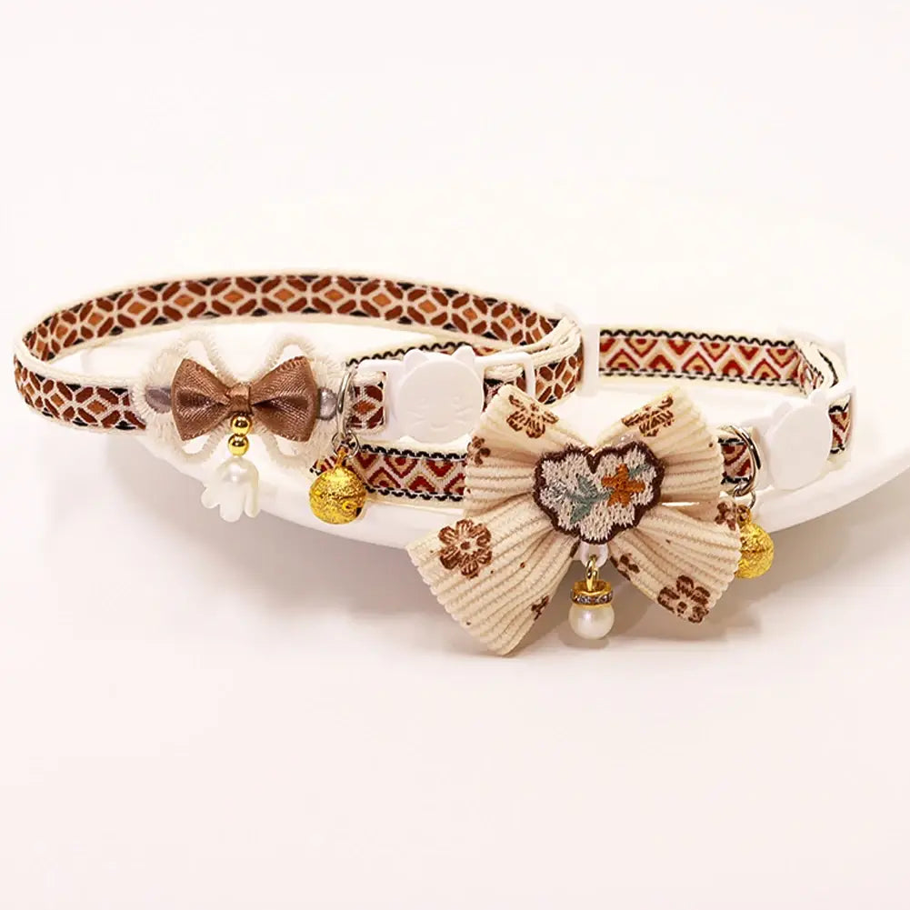 adjustable floral cat collar with bell featuring two decorative collars with adjustable length, one with a brown satin bow and the other with an off-white pleated fabric bow adorned with floral embroidery.