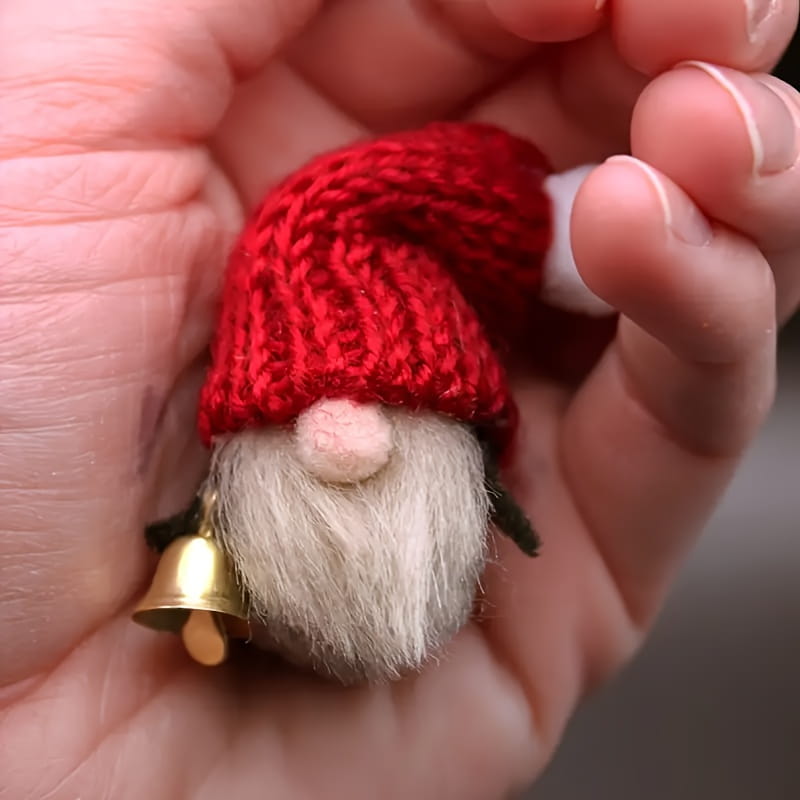 Une minuscule breloque de petit gnome en tricot rouge, avec une barbe blanche duveteuse et une clochette dorée, faisant partie d’un ensemble de clochettes de traîneau en métal doré de 20 pièces.