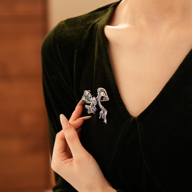 Eine funkelnde silberfarbene Schmetterlingsbrosche, verziert mit grünen und klaren Kristallen aus der Kollektion „Zircon Bow Brooch“ im luxuriösen französischen Design.