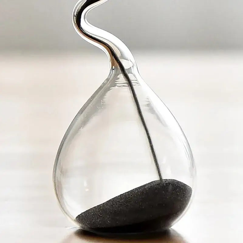 a sleek transparent glass sand timer hourglass with a curved neck and black sand flowing through it used as home decoration
