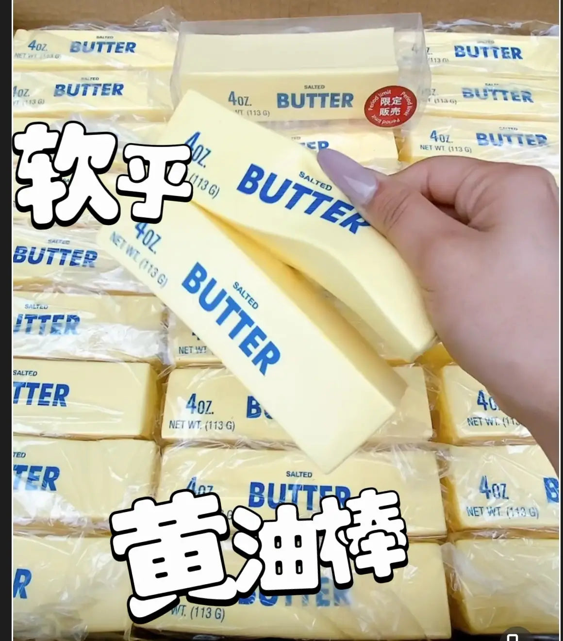 Una mano sostiene un juguete antiestrés blando con forma de barra de mantequilla, de color amarillo pálido, que asciende lentamente, en un envoltorio de plástico transparente con letras azules de mantequilla.