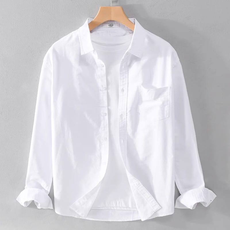 A crisp white durable casual men’s long sleeve work shirt made of breathable fabric with a classic collar and rolled cuffs hanging neatly on a wooden hanger.