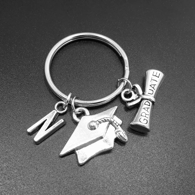 Silberner Schlüsselanhänger zur Abschlussfeier mit einem Anhänger in Form des Buchstabens n, einer Abiturmütze und einem mit Graduate gravierten Diplom – ideal zum Feiern akademischer Leistungen.
