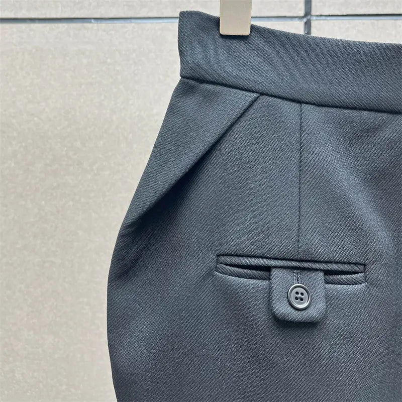 Pantalon en tissu texturé gris foncé comportant une poche à rabat fermée par un bouton, vue depuis l’arrière, assorti à une jupe crayon grise taille haute de longueur genou au style Y2K.