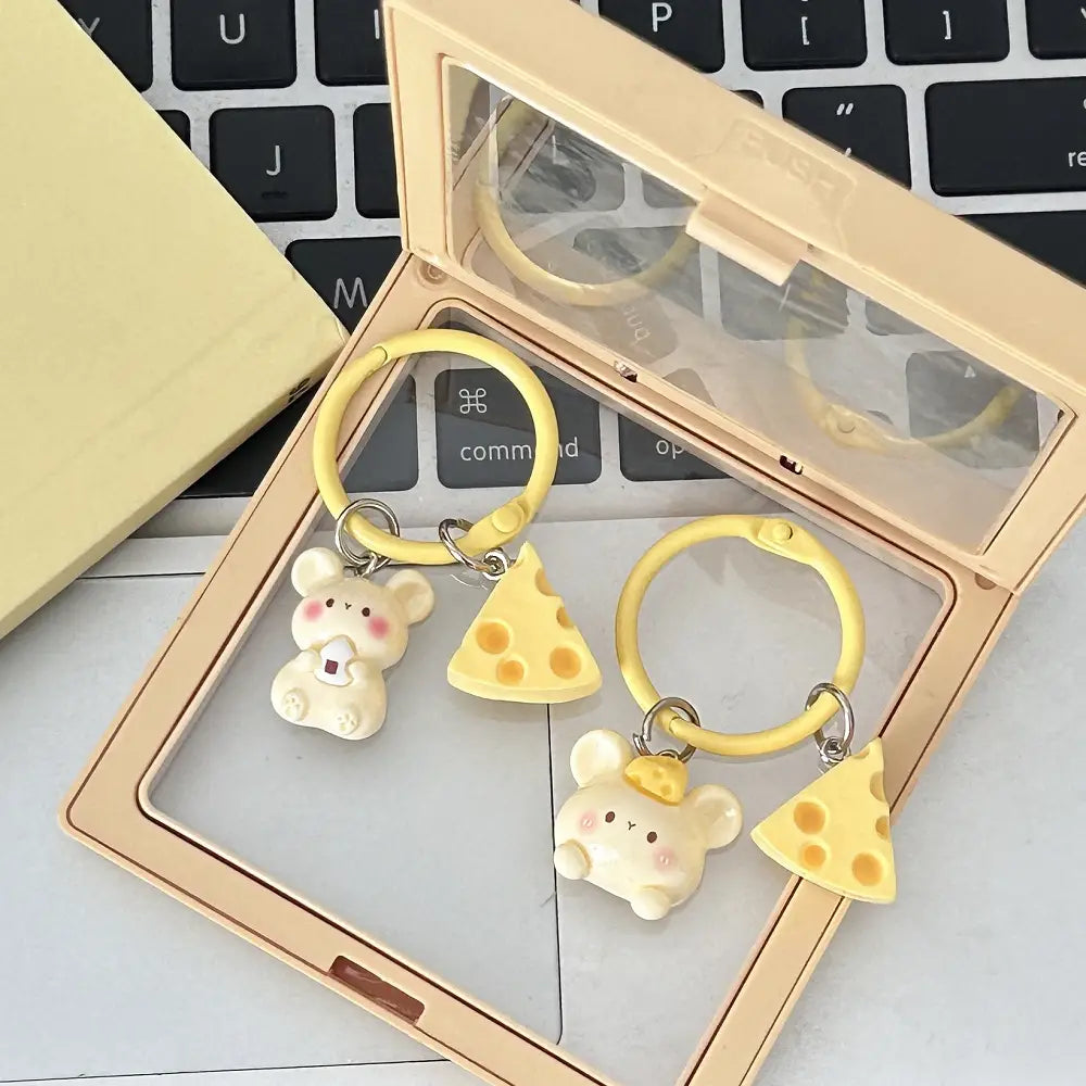 Two yellow keychains featuring cream-colored kawaii mouse figurines holding or standing beside cheese-shaped charms as bag charms.