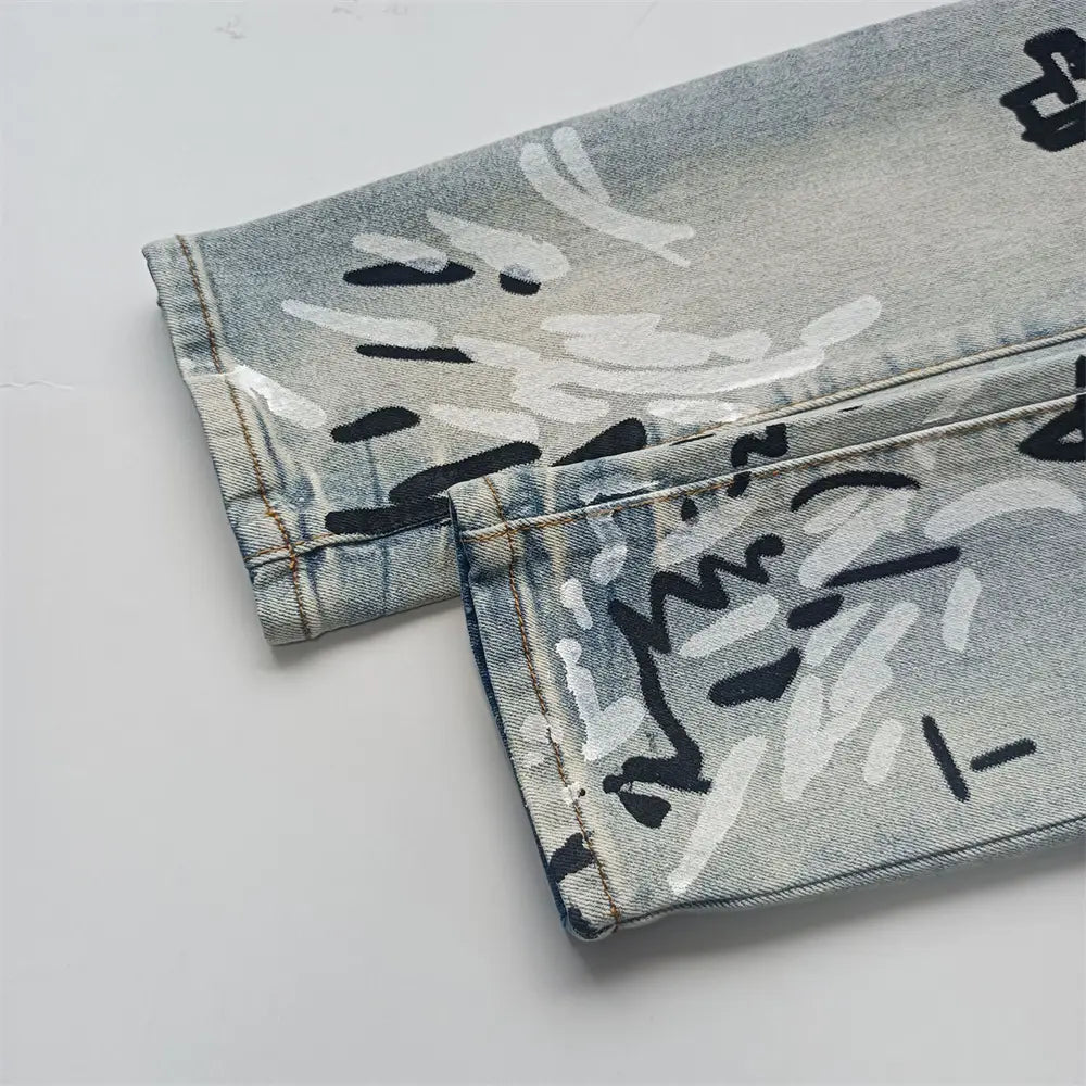 Jeans skinny déchirés pour hommes en denim à lavage clair, avec une lettrage de type graffiti noir et blanc audacieux sur l’ensemble du tissu.