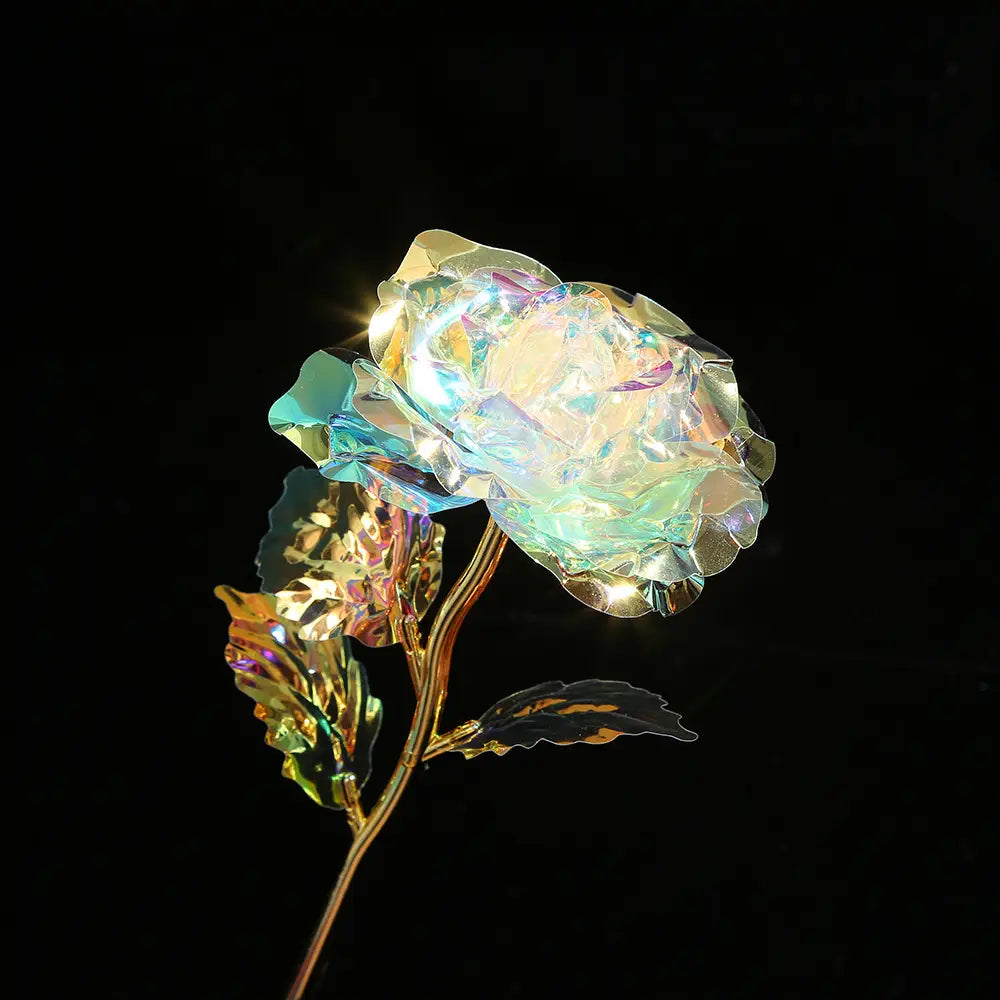 Iridescent crystal rose with golden stem and leaves glowing softly against black background in gold foil artificial rose eternal gift flower.