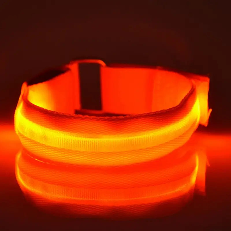 Un brazalete de seguridad LED recargable por USB naranja luminoso para correr, con hebilla negra y franjas reflectantes, para iluminación de seguridad.