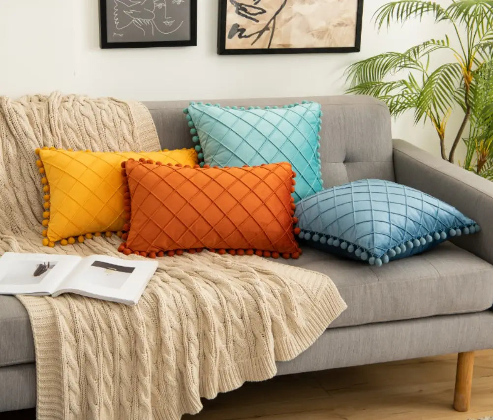 ensemble de quatre housses de coussin matelassées colorées en jaune, orange, bleu canard et bleu, avec garniture à pompons, adaptées à des retours positifs pour la housse de coussin en velours gris avec pompons.
