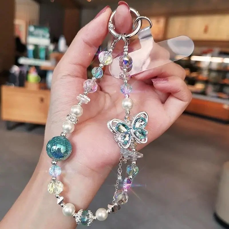Une délicate breloque papillon argentée ornée de cristaux bleus scintillants et transparents, suspendue à une chaîne pour téléphone mobile, comportant des perles en verre irisé et des accents de perles.
