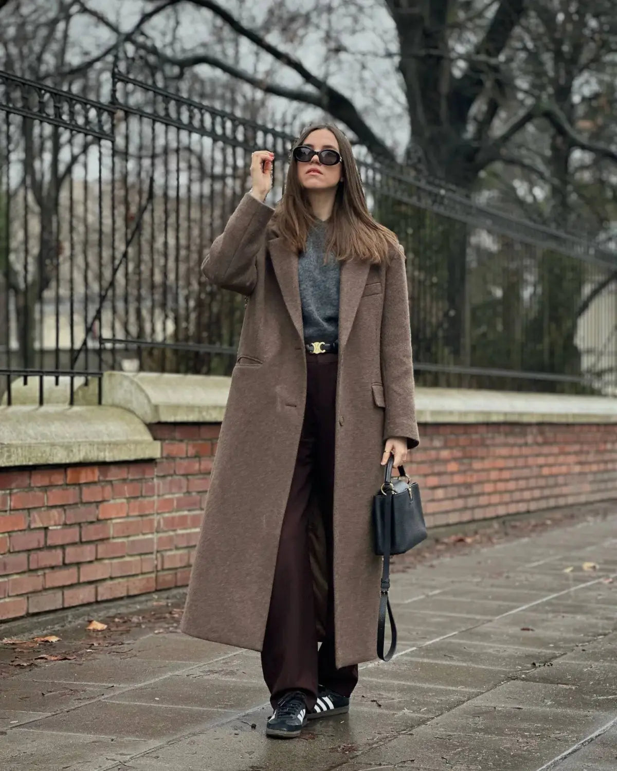black structured handbag with slender strap and minimalist design paired with a brown wool blend overcoat for women winter commuter jacket.
