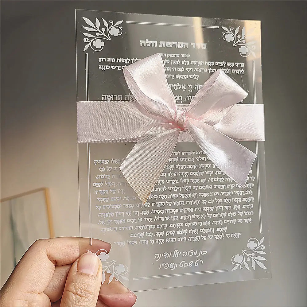 Custom Hebrew acrylic prayer card featuring delicate translucent material with elegant white floral etchings and a soft pink satin ribbon bow for wedding and bar mitzvah souvenirs.