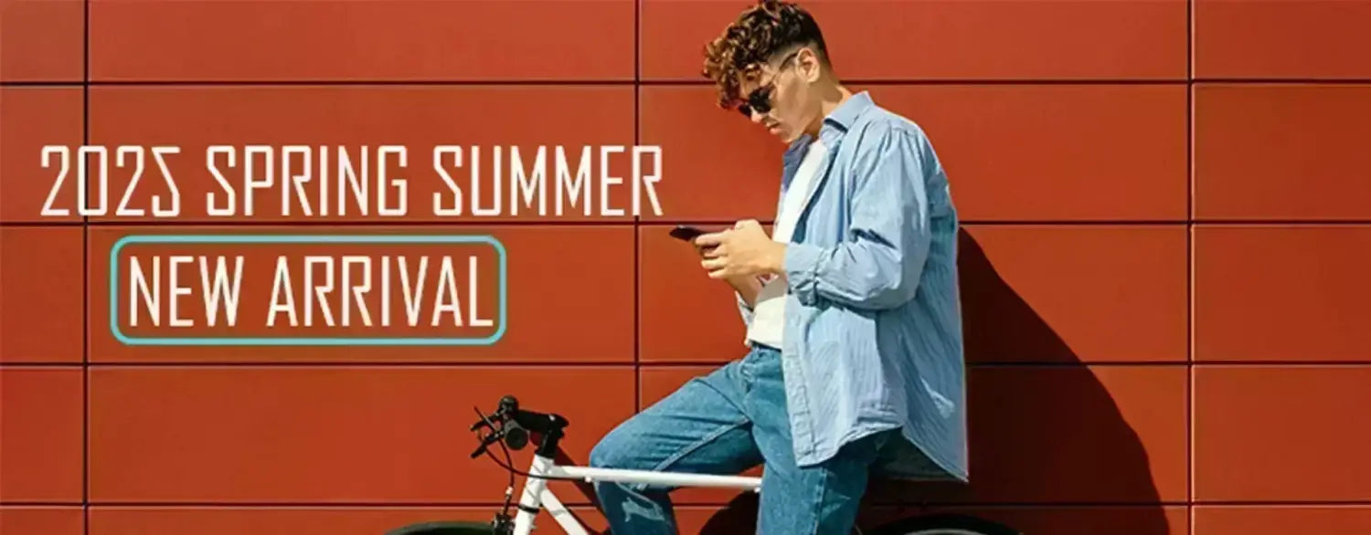 A man in a light blue denim shirt and jeans leans against an orange tiled wall holding his phone beside a white bicycle wearing a funny quote novelty graphic tee shirt.