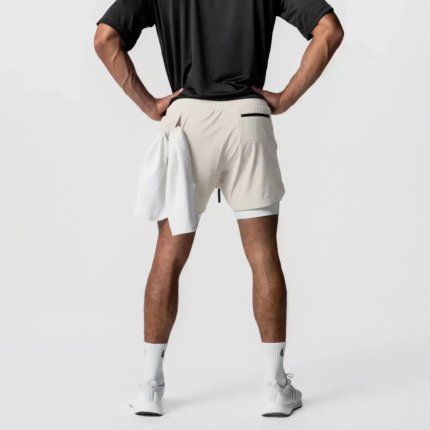Hombres, pantalones cortos atléticos de dos capas para gimnasio color beige con bolsillo con cierre negro, detalles sutiles en la costura lateral y una trabilla para la toalla que ofrece soporte durante los entrenamientos.