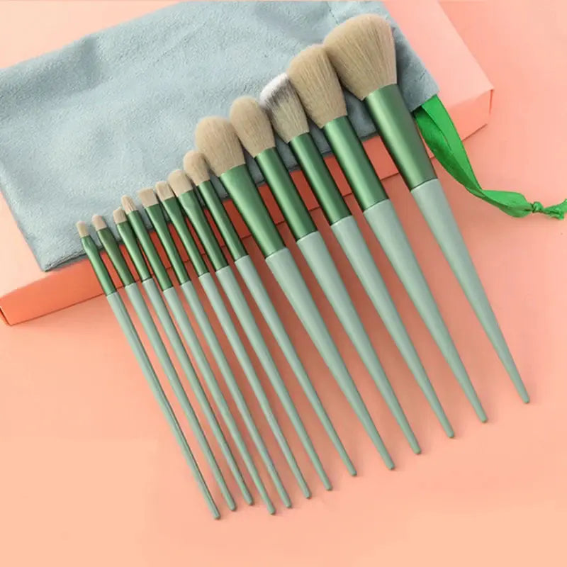 Set aus 15 professionellen Make-up-Pinseln mit mintgrünen und salbeigrünen Griffen und weichen beigen Borsten, ordentlich in einem hellblauen Microfaserbeutel angeordnet.