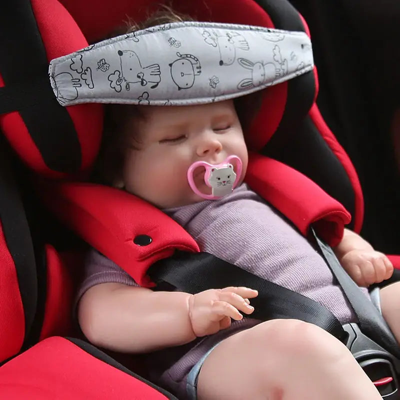 Kopfstützriemen für einen Babyschalen-Sitz verstellbarer Schlafpositionierer aus grauem Stoff mit schwarzen Cartoon-Tiermotiven, getragen von einem Baby in einem roten Autokindersitz.
