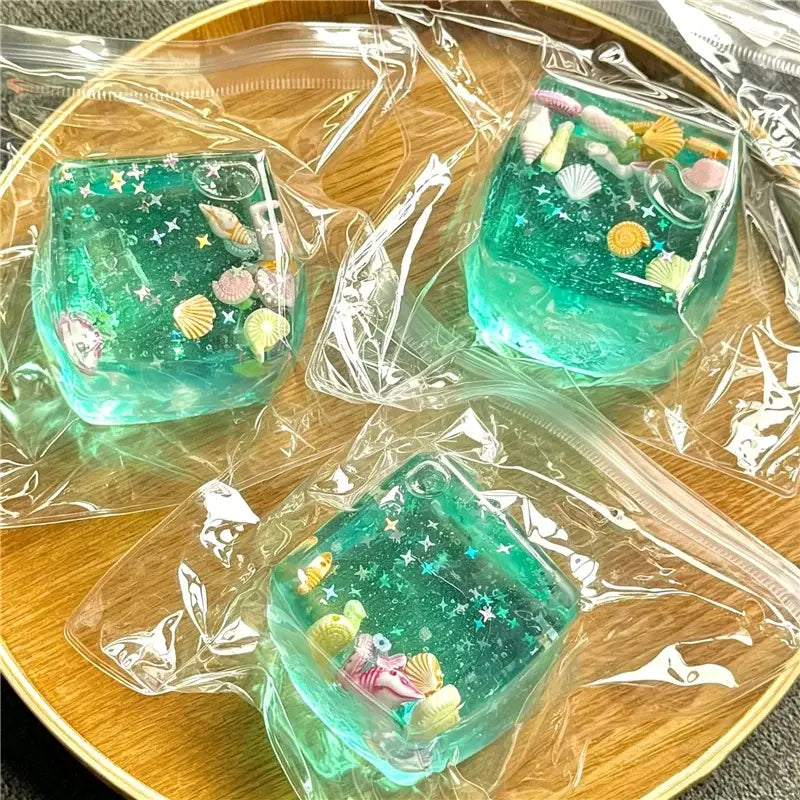 trois cubes sphériques translucides à faible rebond, visqueux et lents, de couleur turquoise, renfermés dans un plastique transparent, remplis d’étoiles scintillantes, de mini coquillages et de petites figurines de poissons, vus de face