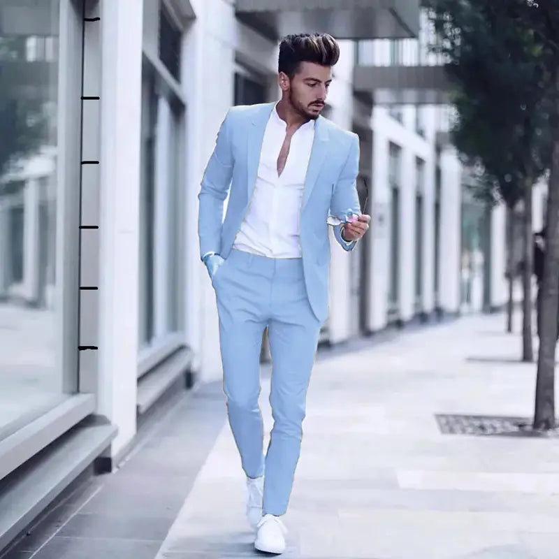 Ein Mann trägt einen hellblauen Slim-Fit-Herrenanzug mit Revers mit Schalkragen und passenden Hosen, kombiniert mit weißen Sneakern, geeignet für Hochzeiten, mit einer einzelnen Knopfleiste als Verschlussart für eine maßgeschneiderte Körpergröße.