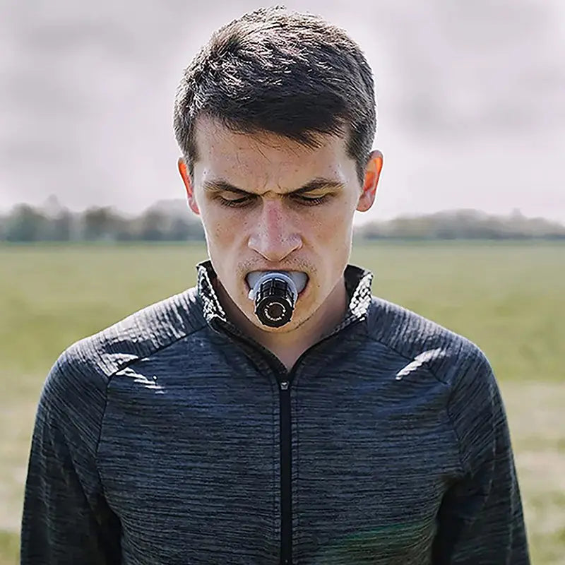 Man holding a black and silver camera lens in his mouth demonstrating lung capacity training device respiratory fitness tool.