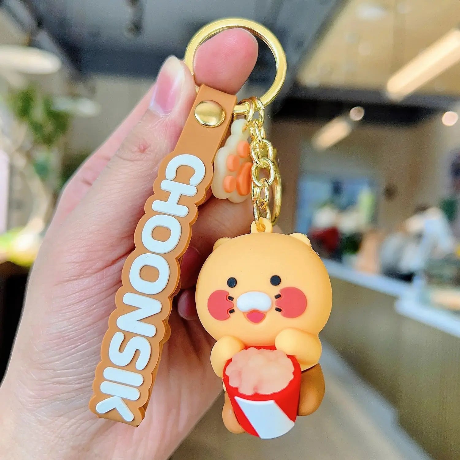 Orange rubber Choonsik silicone scooter keychain featuring a cute cartoon bear holding popcorn with white lettering on the strap as a Korean viral gift.
