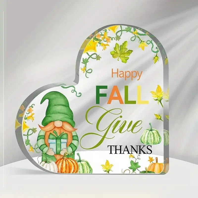 Ein Acryl-Weihnachtsherz-Ornament-Desktopständer mit einem herzförmigen Deko-Schild, auf dem ein grün gekleideter Gnom ein Geschenk hält, umgeben von Kürbissen und Herbstblättern in Orange-, Gelb- und Grüntönen.