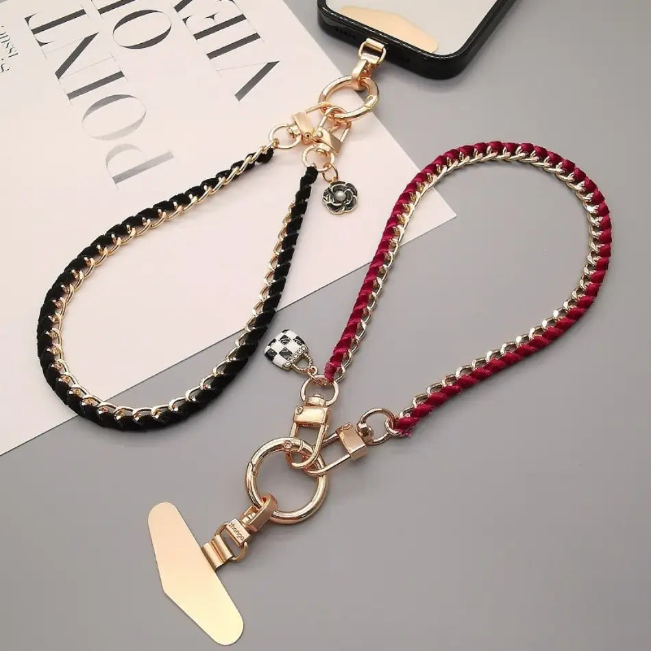 Zwei geflochtene Handy-Handgelenkriemen in Schwarz und Rot mit goldfarbenen Metallbeschlägen und dekorativen Anhängern, entworfen als Anti-Lost-Handylanyards.