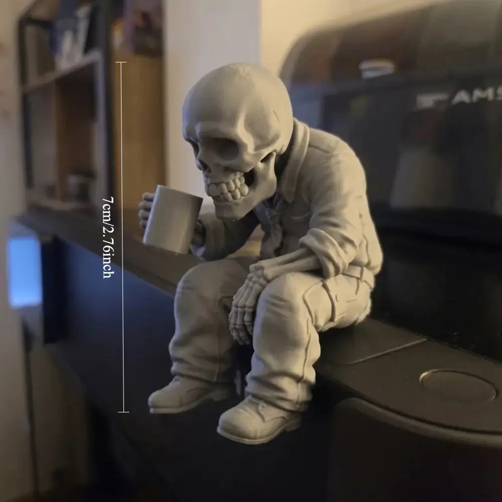 A gray detailed skeleton coffee desk figurine dressed in a suit sitting and holding a mug as an office ornament.