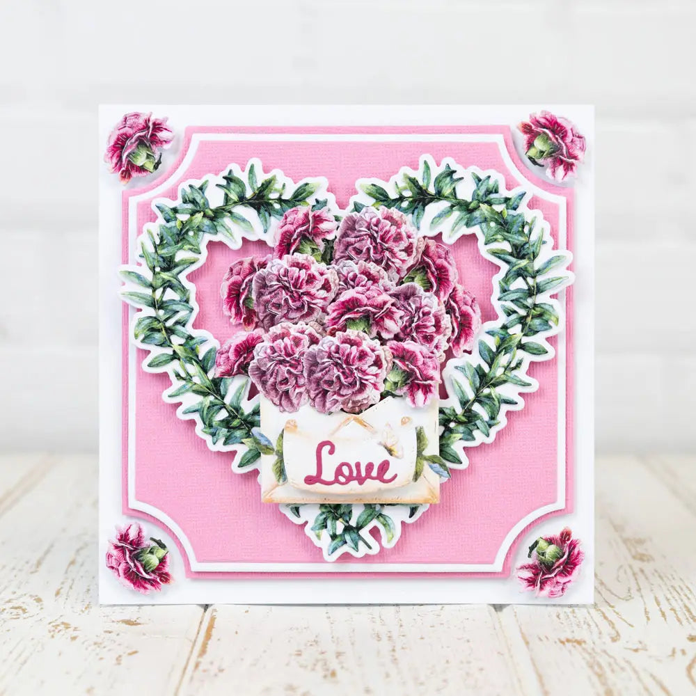 Valentine metal cutting die features a pink floral heart shaped card with layered paper cutouts of deep pink carnations and greenery accented by a small love tag for diy cards.