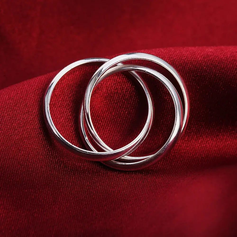 Three interlocking sterling silver rings with a smooth polished finish rest on rich red fabric in the women simple three circles design.