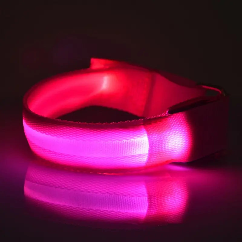Un brazalete de seguridad LED recargable por USB rosa luminoso para correr, con correa flexible de tela texturizada y hebilla ajustable.