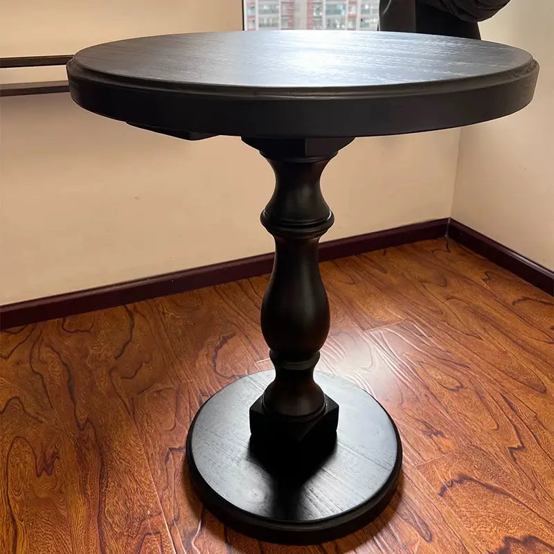 Black wooden pedestal round accent table featuring a turned pedestal base and circular foot made of wood.