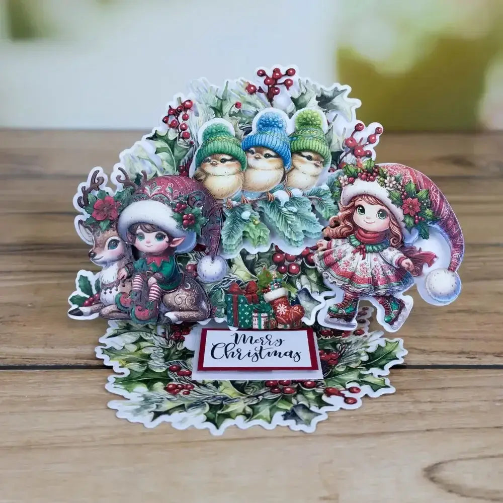 A festive christmas metal cutting die and stamp set featuring a pop-up card with illustrated characters in winter attire adorned with holly and berries.