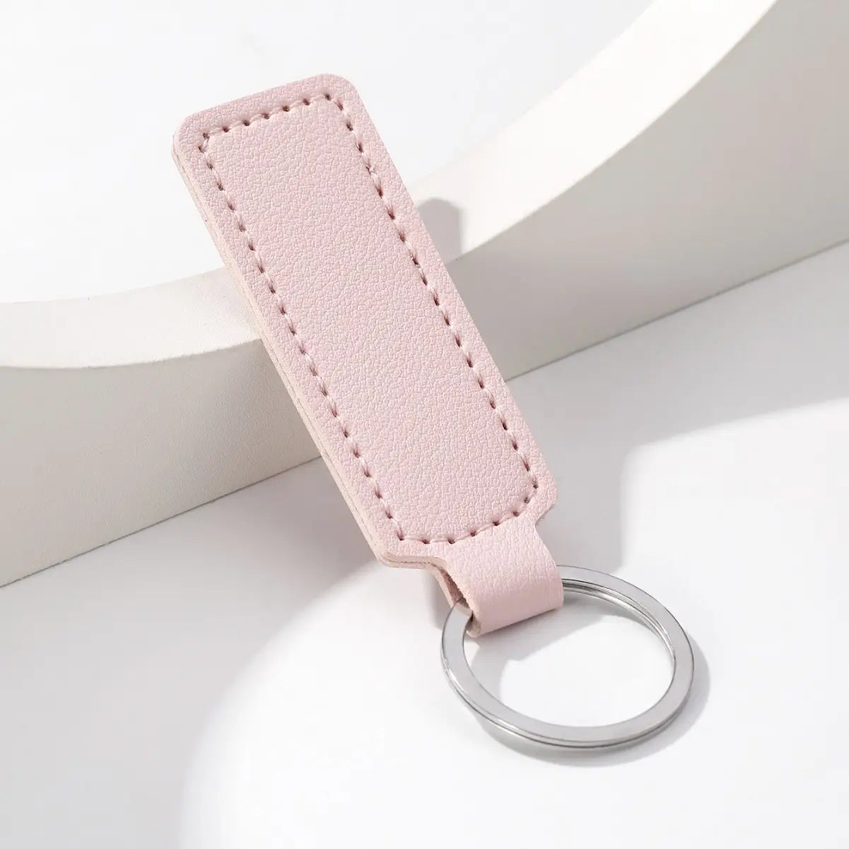 A delicate blush pink leather car keychain minimalist strip key ring with a sleek silver metal ring.