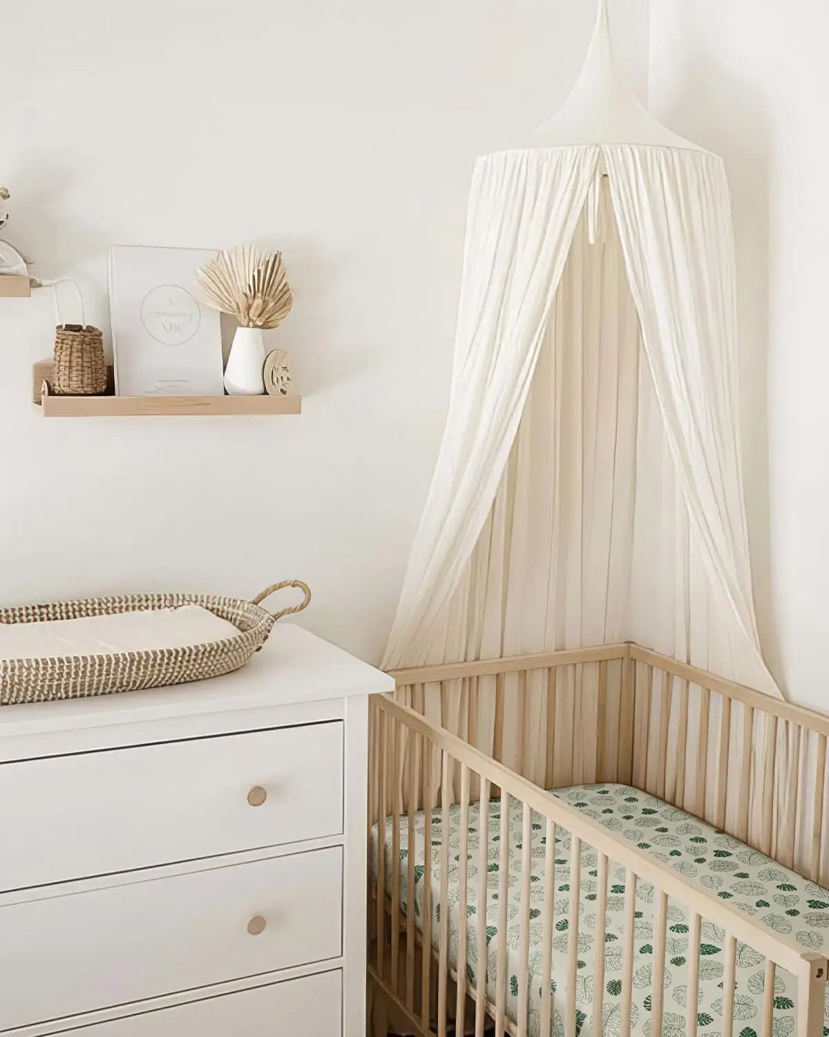 ein weicher, off-white durchscheinender Baumwollmuslin-Himmel mit sanft zulaufender Oberseite und fließendem Stoff, der über die Ecke eines Holz-Babygitters drapiert ist.