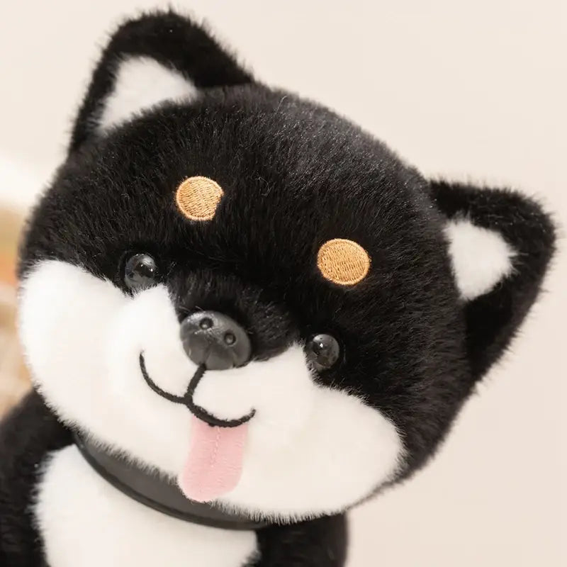 A plush black and white Shiba Inu dog stuffed animal toy with embroidered gold patches on its forehead, a pink tongue sticking out, and stitched facial features.