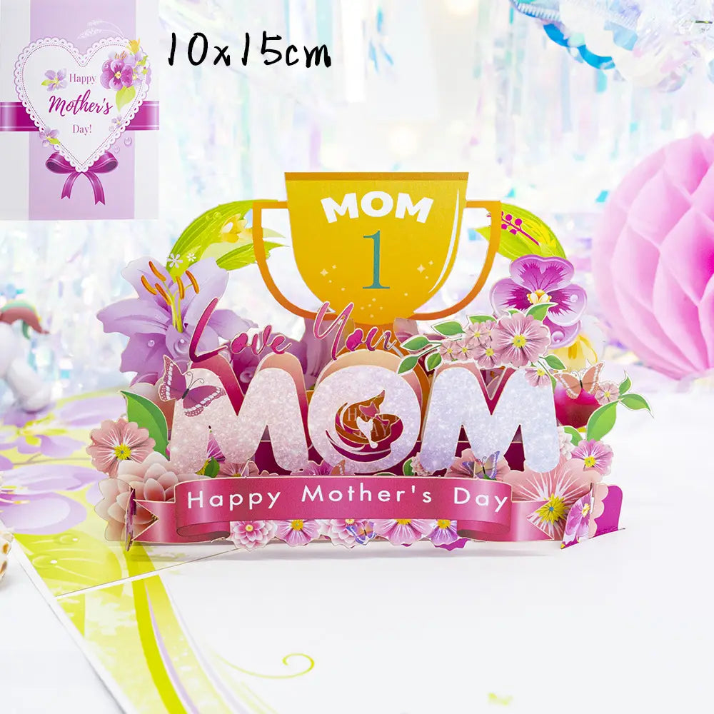 A vibrant three-dimensional Mother’s Day 3d pop up flower bouquet greeting card featuring glittery white mom letters surrounded by pink and purple flowers, butterflies, and a golden trophy inscribed with mom 1.