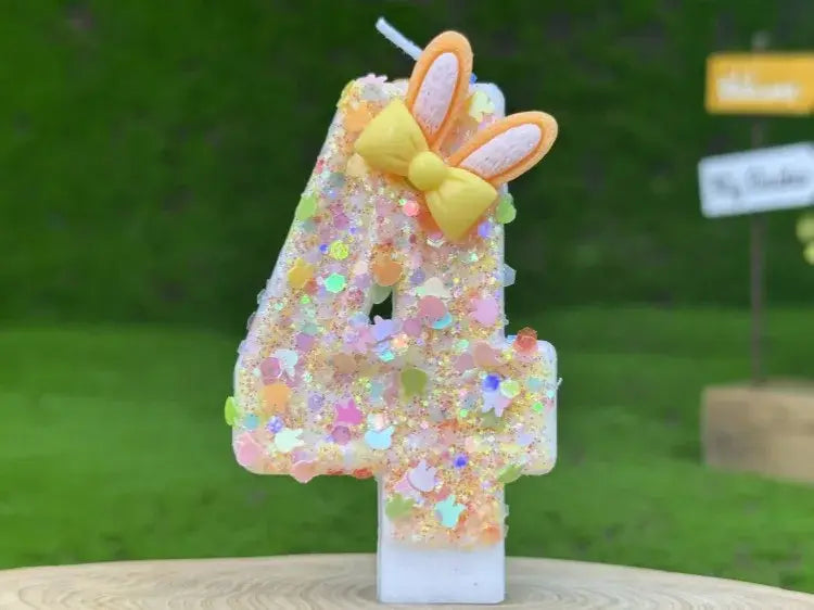 A glittery pastel-colored number four birthday candle with a yellow bow and orange bunny ears designed for birthday celebrations.