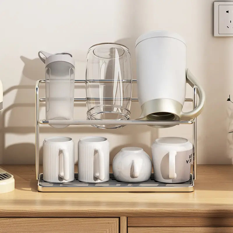 Stainless steel two-tier mug and cup storage rack holding white ceramic mugs, a clear glass pitcher, and a white insulated water bottle.