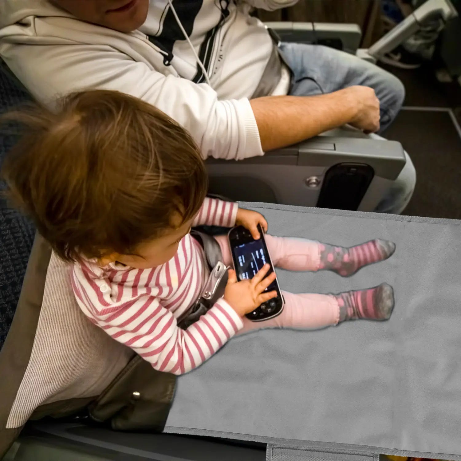 幼児用飛行機用シートエクステンダー、旅行フットレストハンモックに取り付けられたグレーの機内シートトレーテーブル。スマートフォンを手に座っている子どもが描かれている