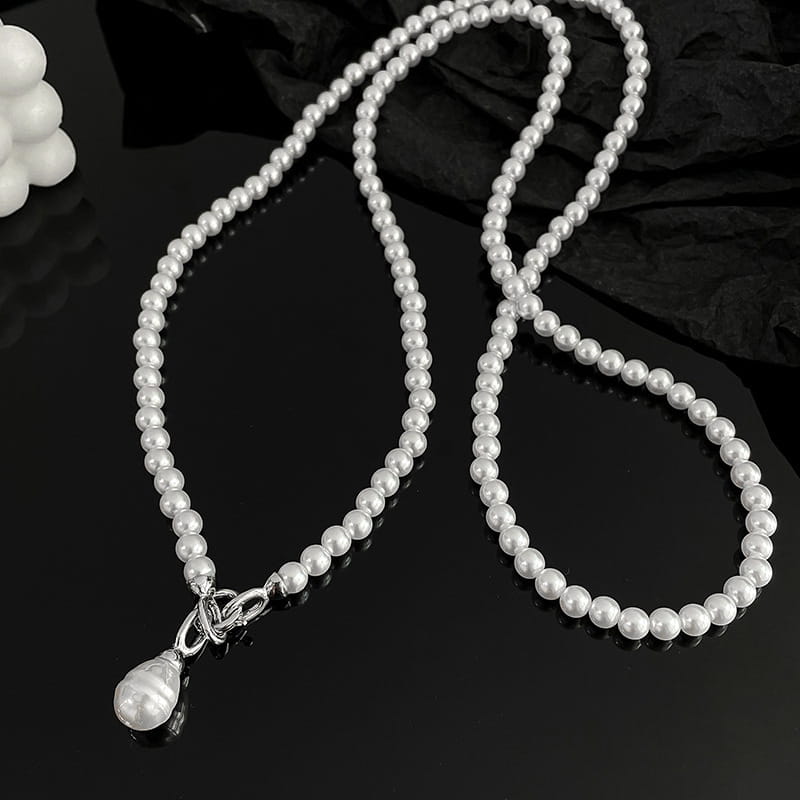 Un long collier en pendentif de perles pour femmes, composé d’un rang délicat de perles blanches uniformes, avec une attache à bascule à l’aspect argenté et un seul pendentif en forme de goutte de perle.